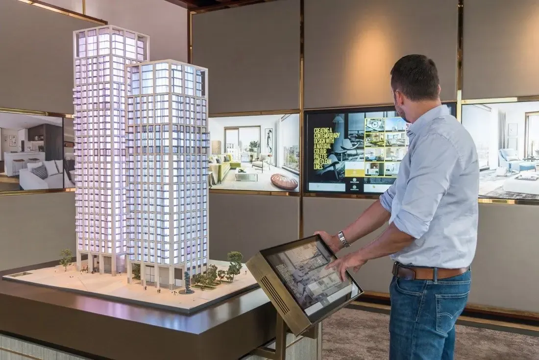 Reference visual of a visitor using a touch screen beside a lit tower model at a property stand