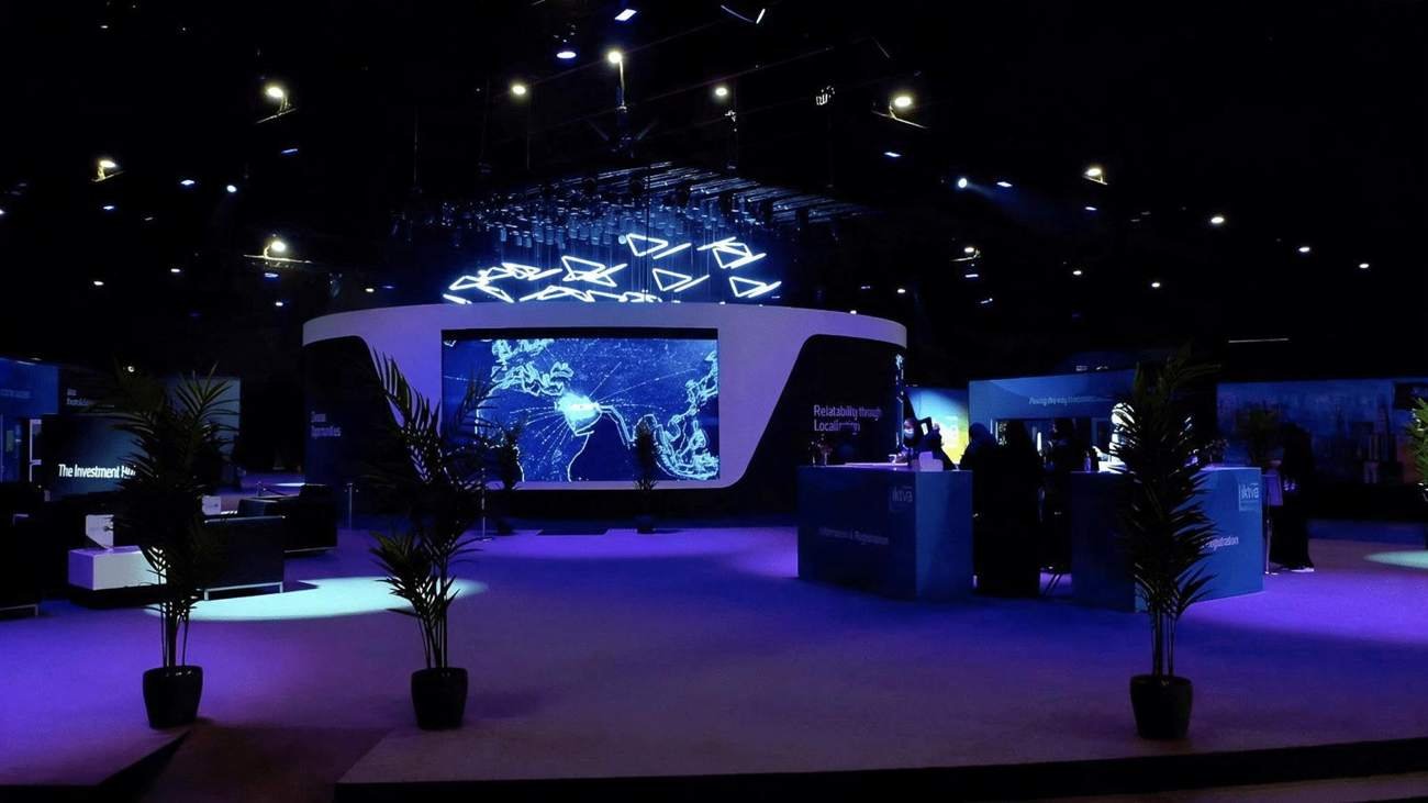 Curved exhibition stand with a large LED world map screen and suspended light sculptures in a dark expo hall