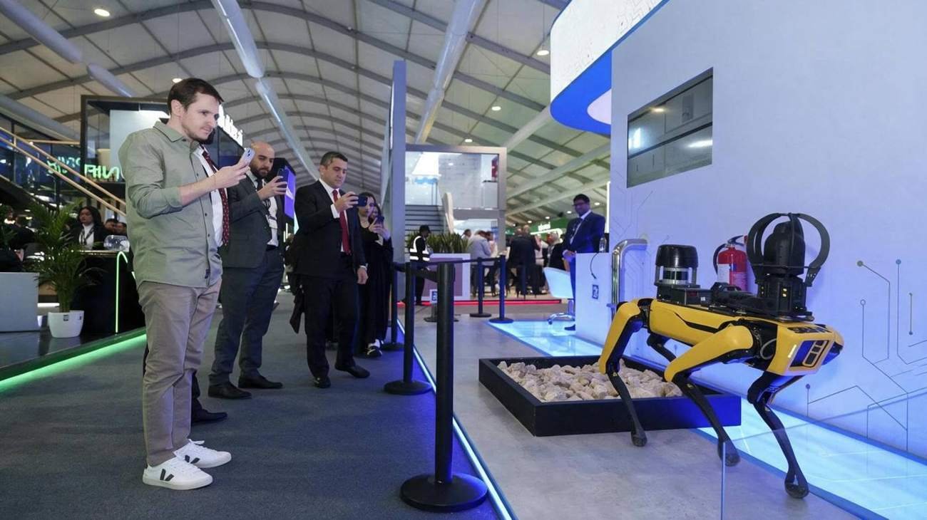Visitors filming a quadruped robot dog on a display plinth inside a modern exhibition hall