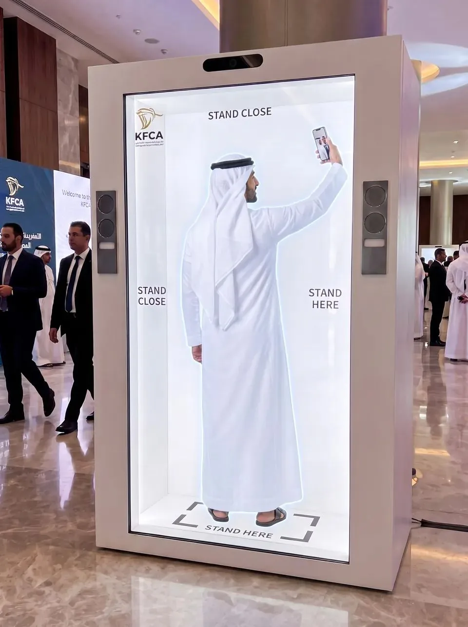 The host inside the cabinet raising his phone to take a selfie, with stand here markers on the screen