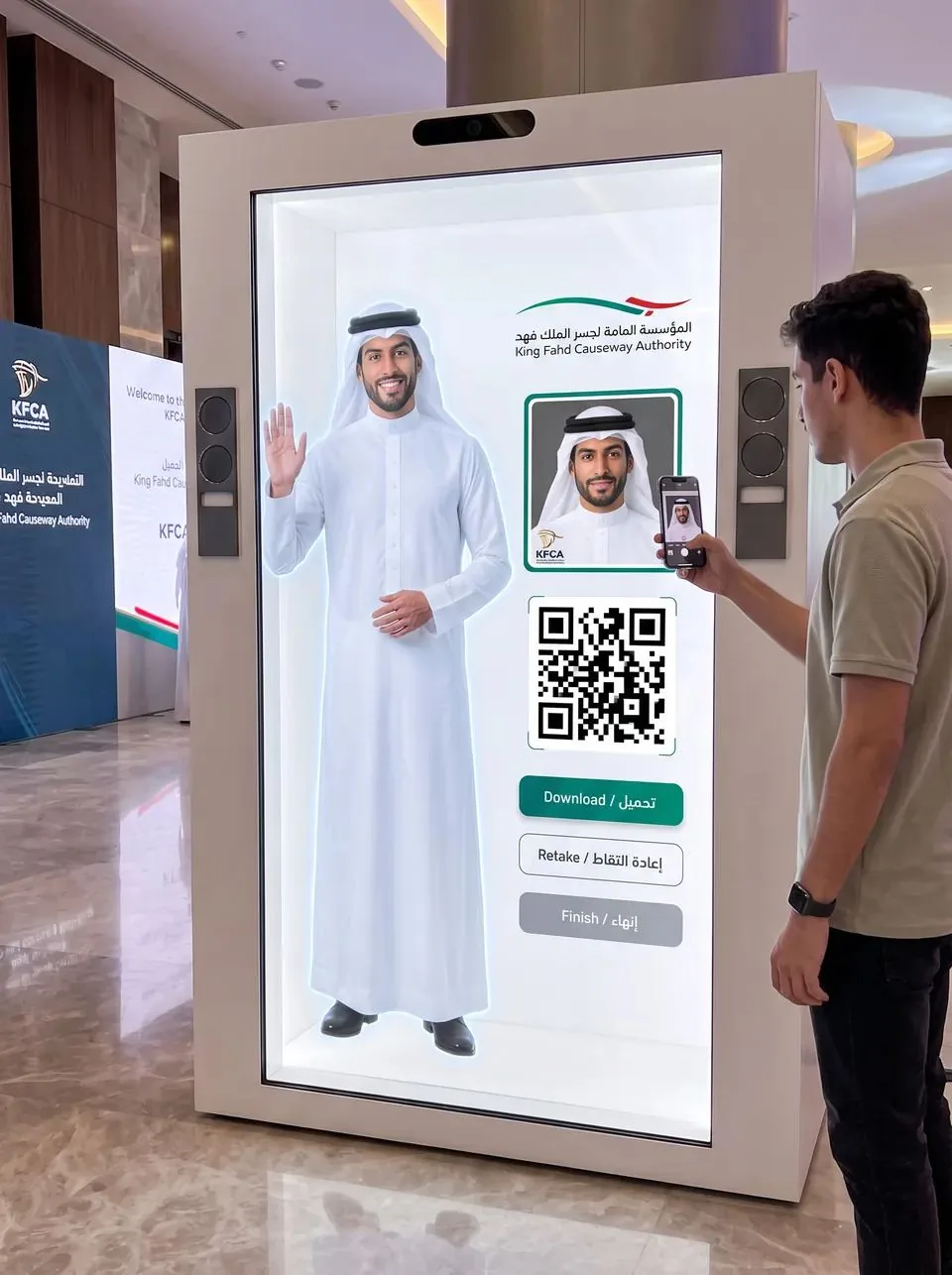 The host waves while the screen shows a framed photo, a QR code and Download, Retake and Finish buttons as a visitor scans the code